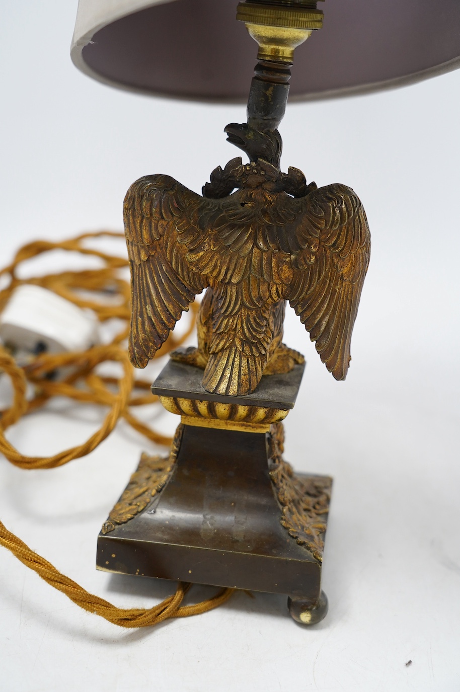 An ormolu table lamp in the form of an eagle with a laurel wreath around its neck, fitted with a grey shade, 39cm high overall. Condition poor to fair, three feet missing to lamp